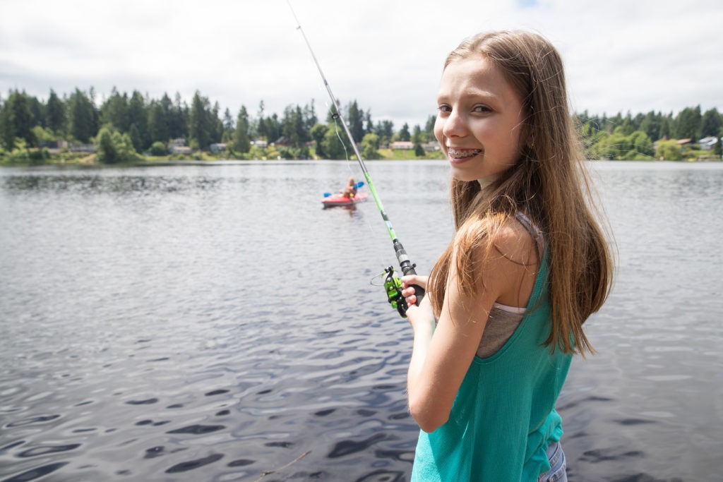 Cute young girl with braces fishing on a lake